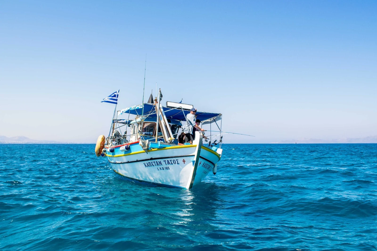 De wit-blauwe vissersboot Kapetan Tasos onder Griekse vlag op helder turquoise water