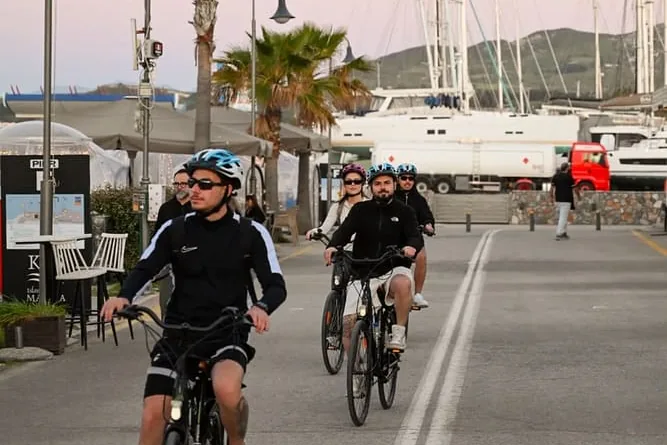 Radfahrende auf der Promenade an der Marina in der Dämmerung, links Palmen, rechts vertäute Yachten
